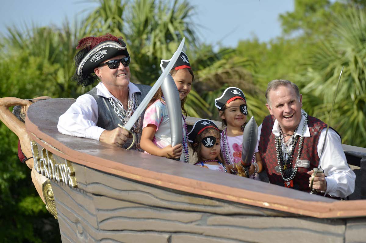 Two men dressed as pirates posing with three young girls wearing eye patches and pirate hats on a 
                pirate ship float